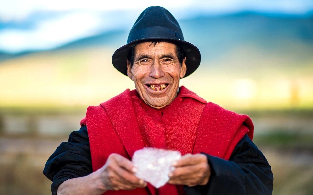 Baltazar Ushca sonriente, con sombrero y poncho rojo, sosteniendo un bloque de hielo
